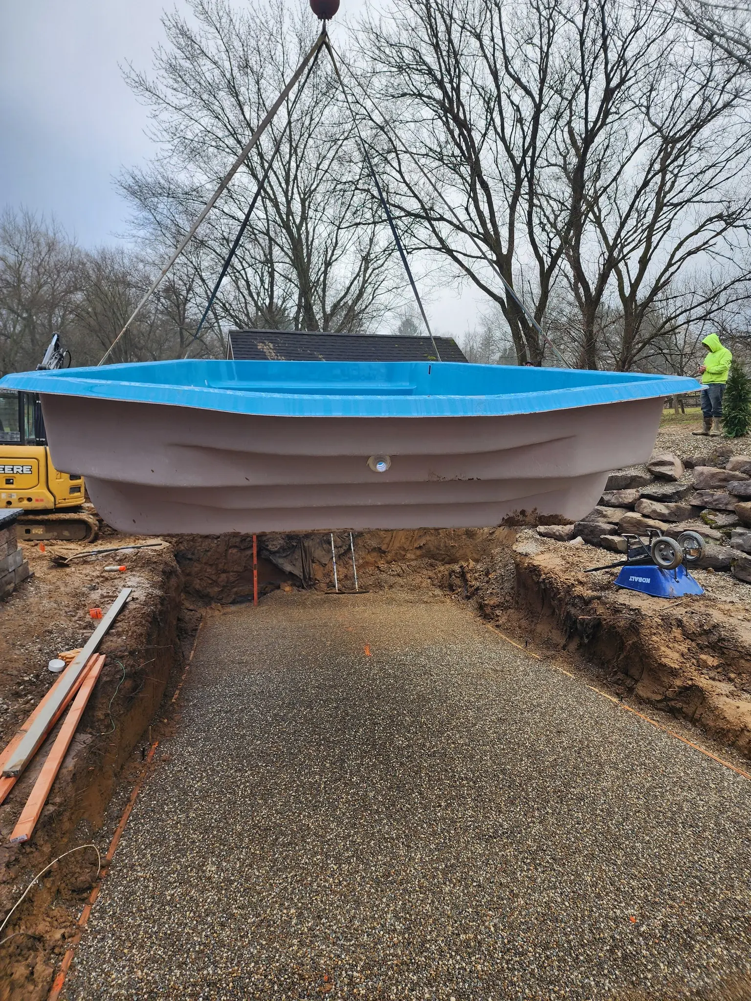 Crane lowering a fiberglass pool shell onto a stone-leveled base
